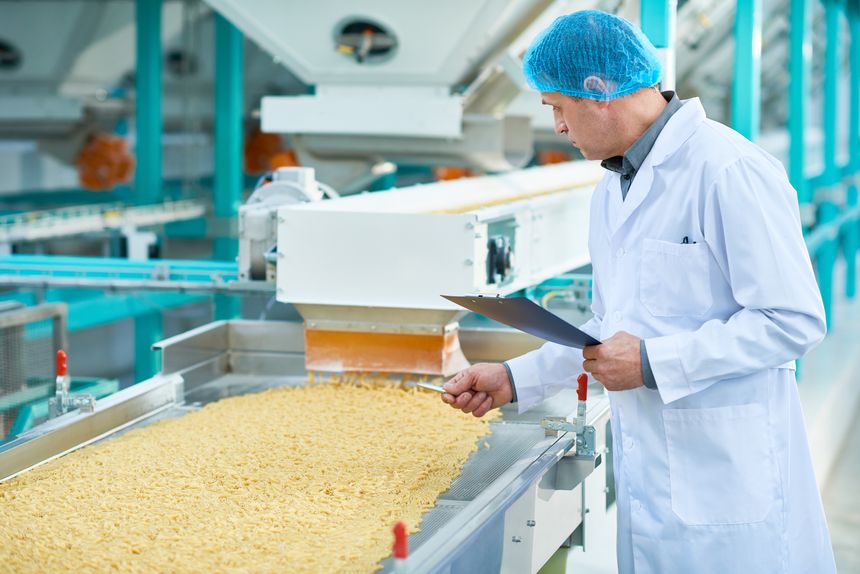 Side view portrait of senior factory worker doing production quality inspection in food industry holding clipboard standing by conveyor belt, copy space