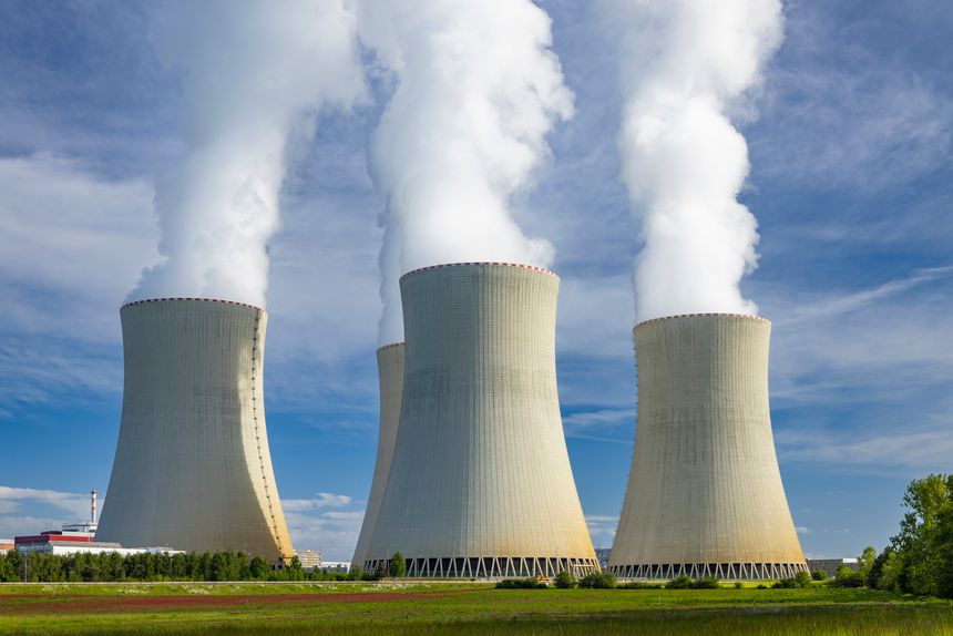 Nuclear power plant cooling towers releasing steam into a blue sky, representing energy production