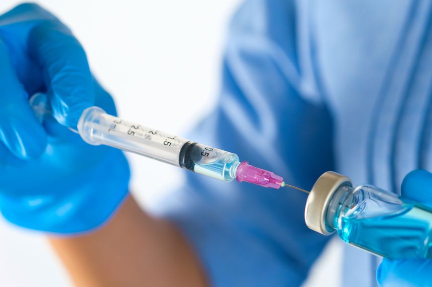Doctor's hand holds a syringe and a blue vaccine bottle at the hospital. Health and medical concepts