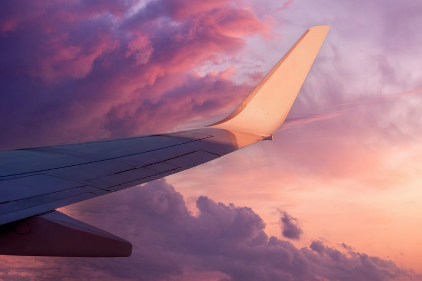View of the wing of a flying airplane in the purple clouds of the setting sun and empty space for text