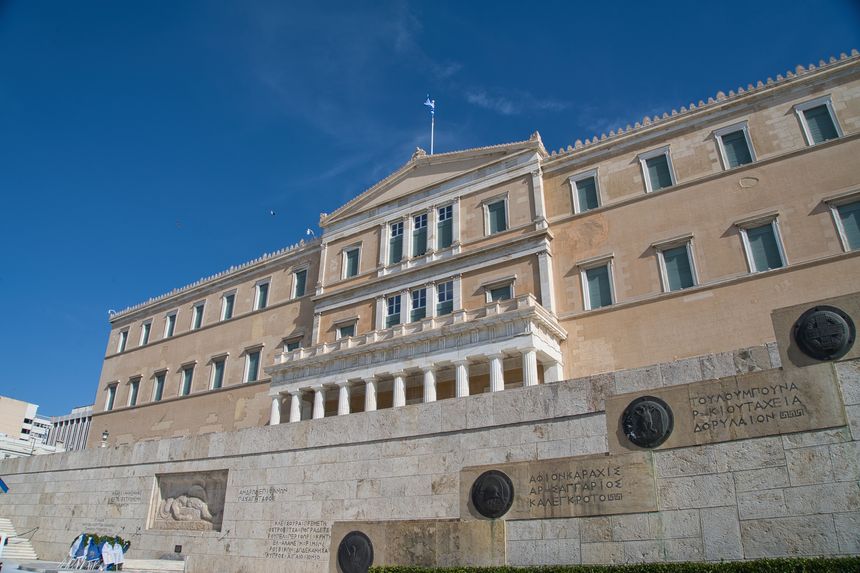 Tourists explore the impressive Hellenic Parliament building in Athens under a clear blue sky, appreciating its neoclassical design and rich history.