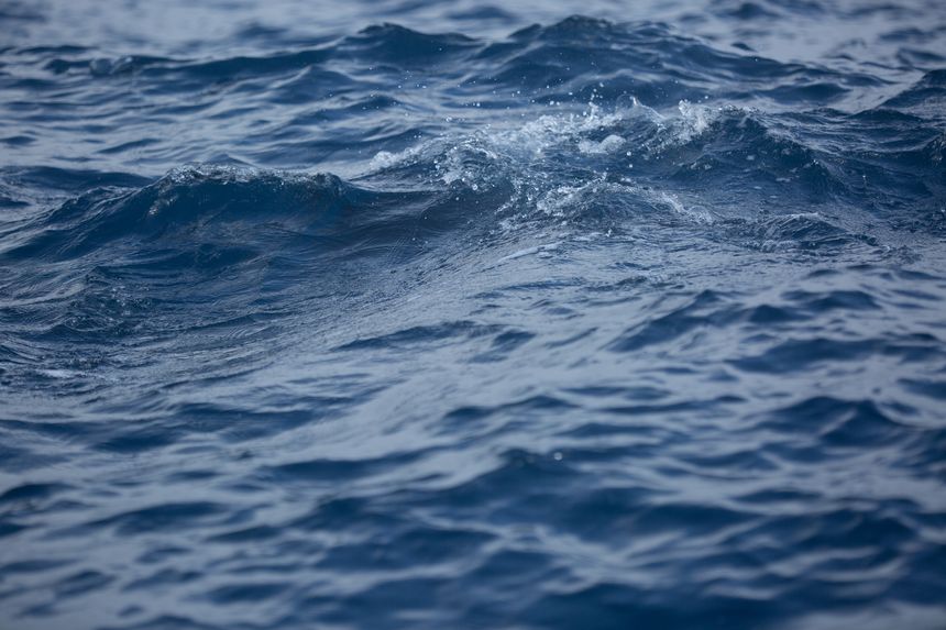 Dynamic close-up of deep blue ocean water with ripples, gentle waves, and subtle splashes creating a natural, textured, and refreshing background.
