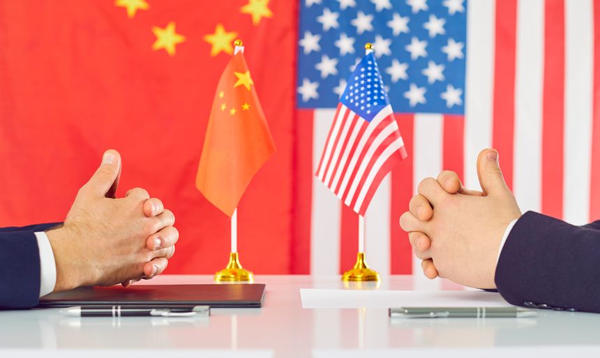 US and Chinese diplomats discuss future strategy and relations between two countries. Close up of hands of men in suits sitting at table facing each other on background of flag of America and China.