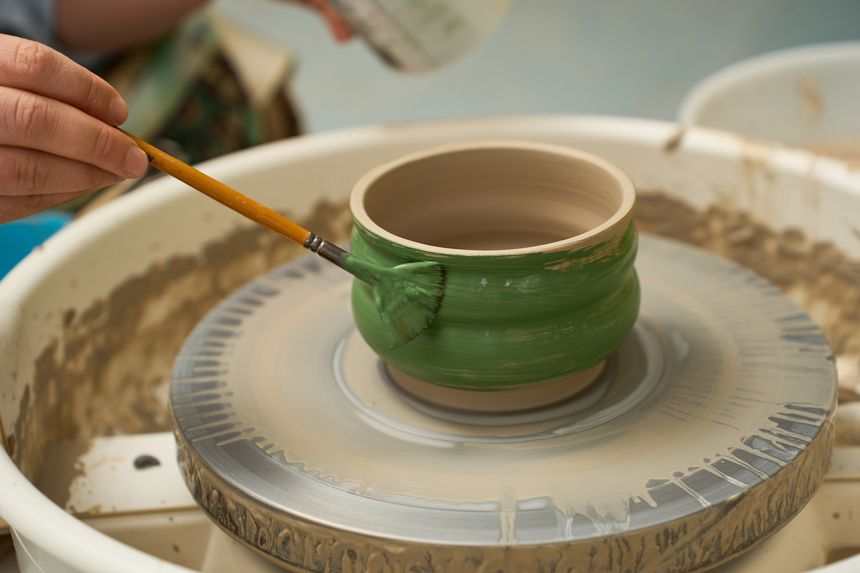 Fine arts studio photography of a potter glazing a round clay bowl with green wash