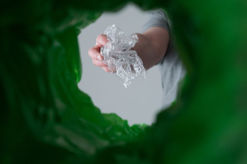 A hand sorting as it holds a crumpled piece of plastic products a green recycling bin at home. Waste segregation, waste sorting, waste recycle. Conscious consumption of plastic. low angle view