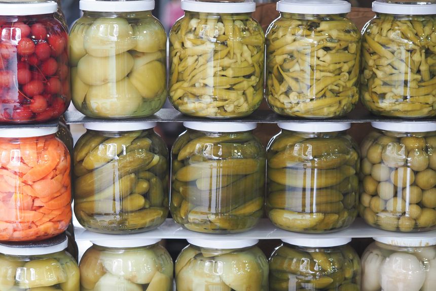 Various pickled vegetables are neatly arranged in jars at a market stand.