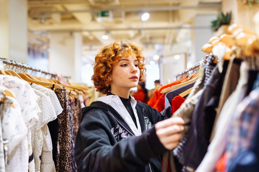 portrait of red-haired attractive young woman trying on clothes in store, buying autumn clothes, shopping