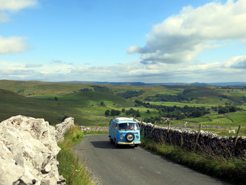 Yorkshire Dales National Park, York, England - July, 24th, 2017: A blue VW Bus from 1973 driving on a very small countryroad with the typical english walls at the side of the pavement and the lush green countryside in the background