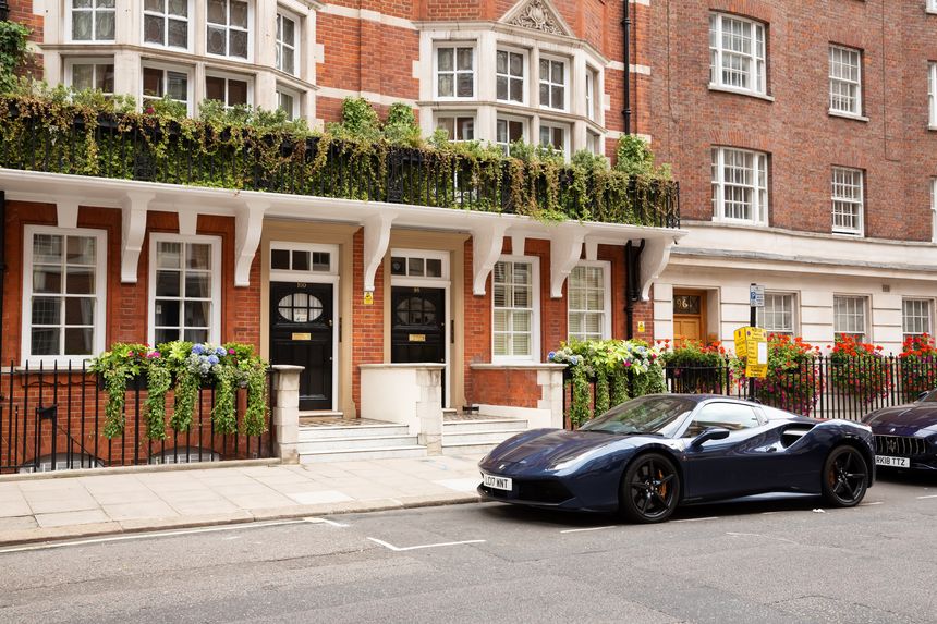 London, United Kingdom - September 23, 2021 - Beautiful blue Ferrari car parked at the old historical building with many plants and flowers.