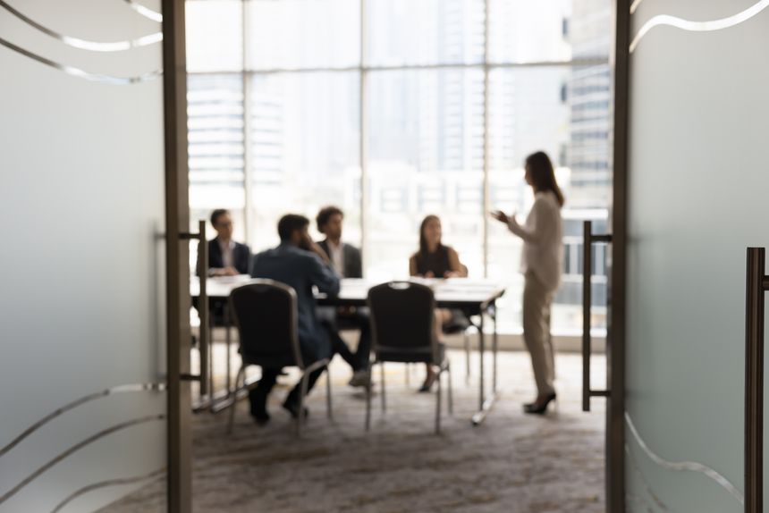 Silhouettes of businesspeople gathered in conference room for negotiation or seminar event, female leader standing inf front of audience makes speech or presentation, blurred view. Business meeting