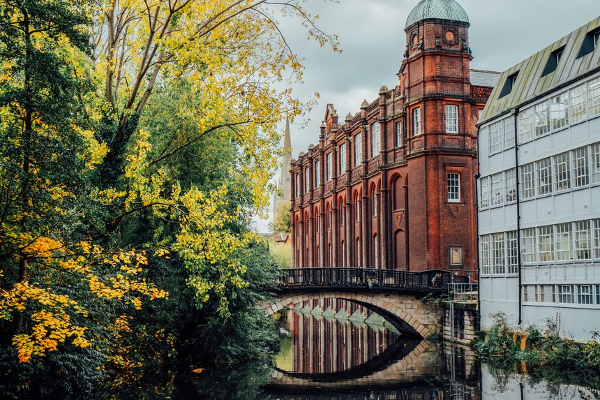 Brick bridge over the river with medieval and industrial buildings and yellow trees background. Norwich City in autumn. Commercial Estate near River In Europe