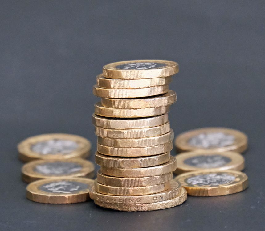 Pile, heap or stack of one and two pound sterling coins. Glowing in a golden light against a dark background. Metaphor for saving, investment, finance and wealth.