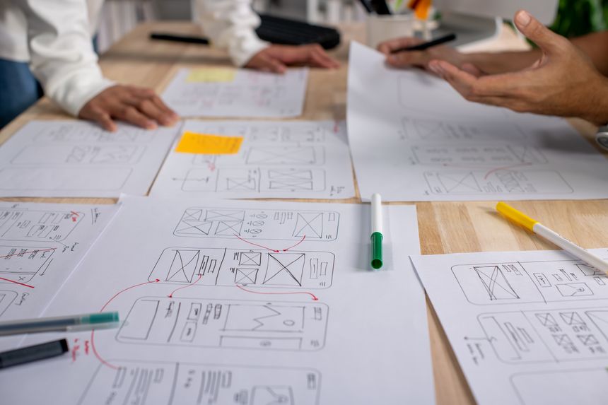 UX UI designers discussing and brainstorming on wireframes for a website and mobile app prototype, surrounded by sketches of user flow and design tools, in the concept of website and mobile application design concept.
