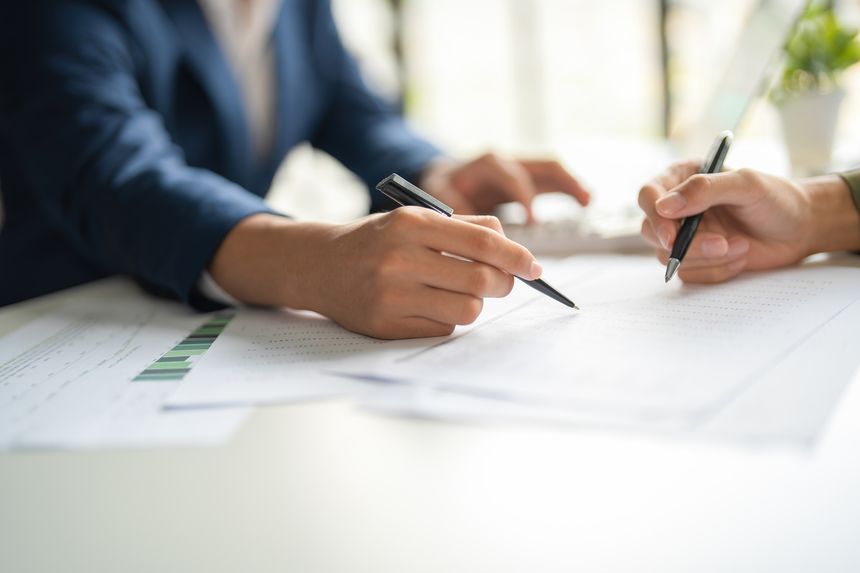 Two businessmen are working together at workplace. They are looking at information while holding pens to discuss about strategies, plans, analytic progress, and financial stats. Business and Teamwork concept.