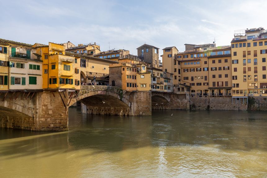 Golden Bridge Reflection Over Calm Arno Waters With Layered Riverside Buildings And Soft Highlights, Tranquil Historic City View Inviting Relaxed Sightseeing In Florence