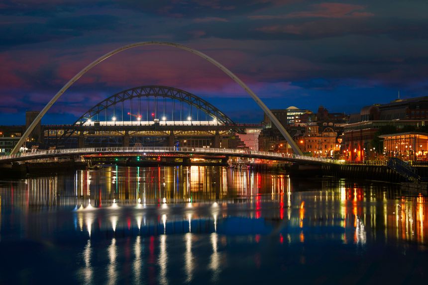 Newcastle city night skyline with Gateshead Millennium Bridge in England. A tranquil riverscape of Quayside with vibrant illuminated water reflections over the River Tyne.