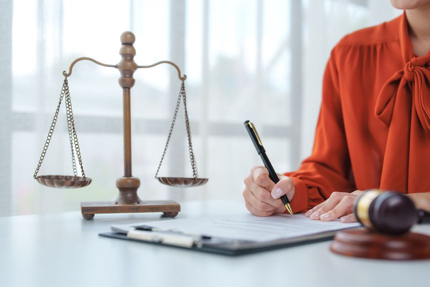 Lawyer signing a legal document with scales of justice and gavel in the background, representing the legal system and justice