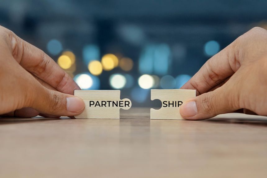 Two hands holding two puzzle pieces to form the word PARTNERSHIP. Collaboration and teamwork concept.