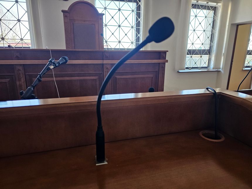 Empty courtroom with a microphone on the witness stand and a wooden backdrop during a hearing or trial session in the afternoon