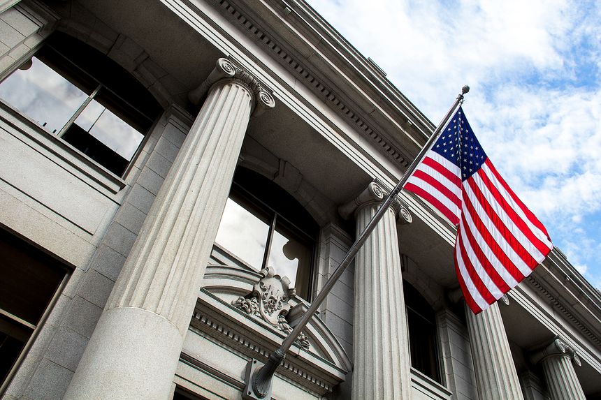 Stone granite official government building in city with American flag waving and flying in the wind, looking up, outside, judicial, freedom, civil courts, columns, criminal justice, law
