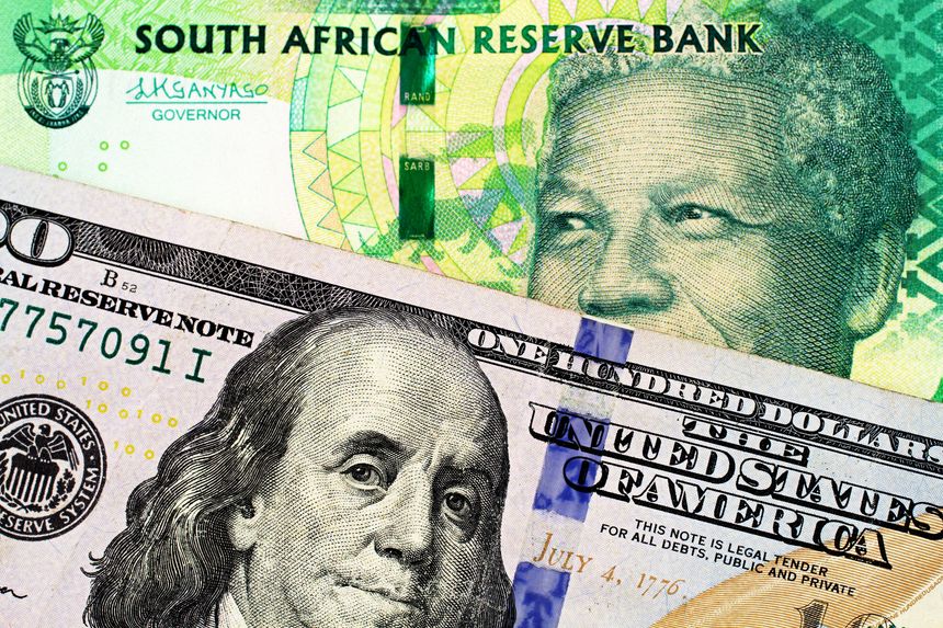 A close up image of a blue American one hundred dollar bill with a ten South African rand bank note
