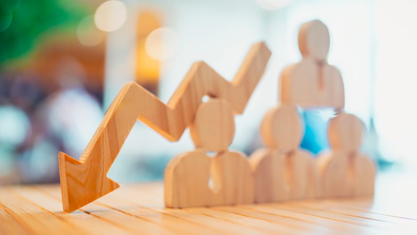 Wooden arrow pointing down over group of people icons representing workforce reduction, employee layoff, HR crisis, or economic downturn. Concept for job loss, downsizing, and business failure.
