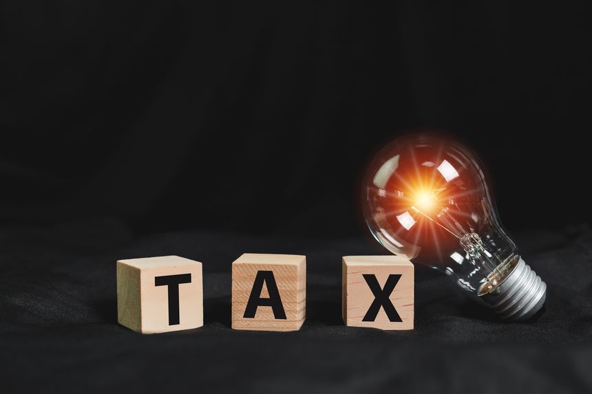 Tax electricity concept. Word TAX letters on wooden cube blocks with light bulb black background. finance invest payment taxation.