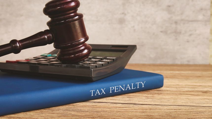 A gavel and calculator on a book titled TAX PENALTY representing financial and legal consequences.