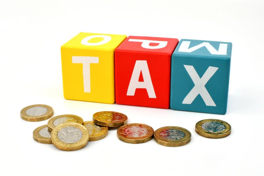 British one pound coins in front of coloured wooden blocks spelling the word Tax isolated against a plain white background