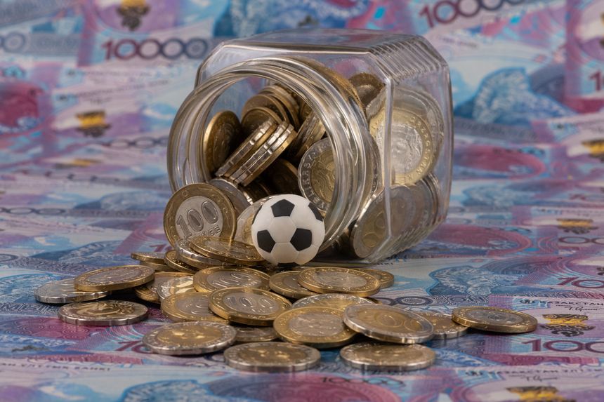 A conceptual story about the financing of Kazakhstani football, featuring a miniature football, 100 and 200 Kazakhstani tenge coins, and 10,000 tenge bills.