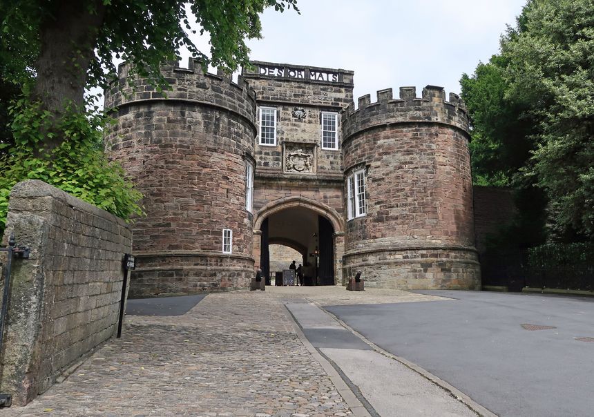Skipton, Yorkshire Dales, United Kingdom, July 3, 2024. Exterior entrance to Skipton Castle with gatehouse towers and cannons. Outdoors, overcast summer day