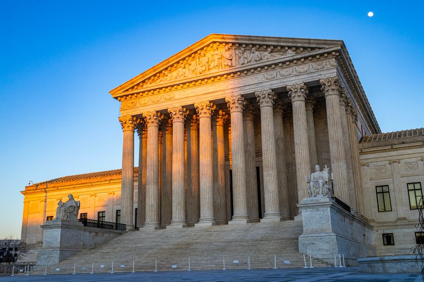 The United States Supreme Court Building at sunset, partly in a shadow cast by the Capitol building, with afternoon light illuminating columns and the