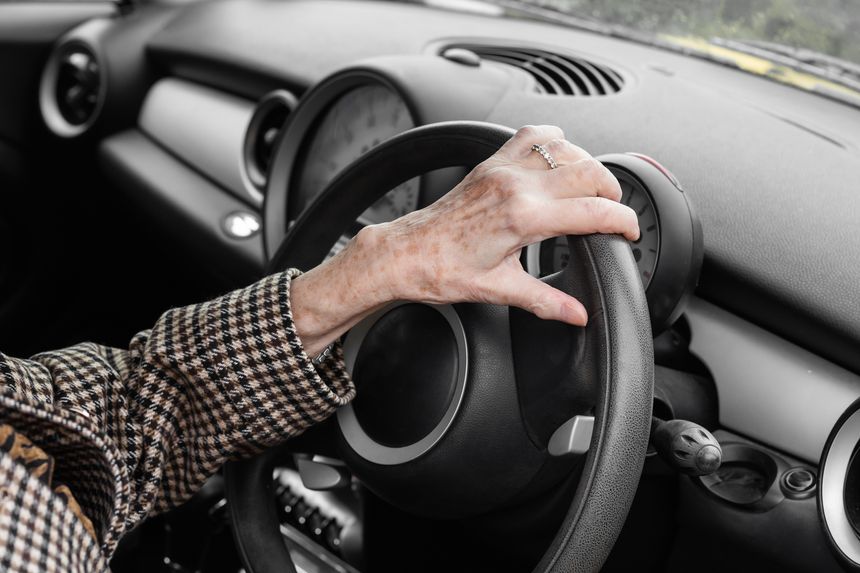 unrecognizable female hand over 80 holding steering wheel, autumn scene from inside a car