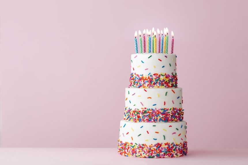 Tiered celebration birthday cake with colorful sugar sprinkles and twelve birthday candles