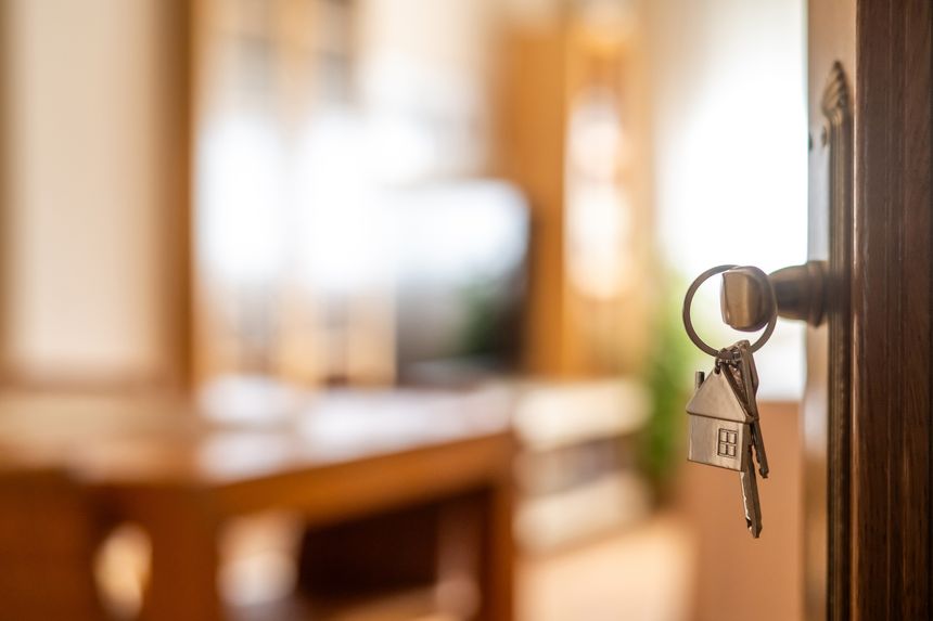 House keys with house shaped keychain hanging on a door, opening to a new home, representing real estate investment, purchase, mortgage and new beginnings