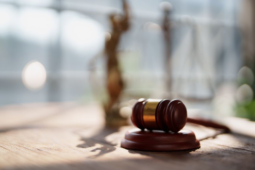 Gavel resting on a wooden desk with a blurred statue of Lady Justice and scales in the background, representing legal process, courtroom decisions, and the concept of balanced justice