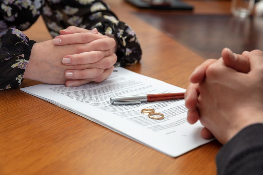 Signing a divorce, marriage dissolution documents and agreement. Wife and husband hands, wedding rings and legal papers for signature on a wooden table, lawyer office