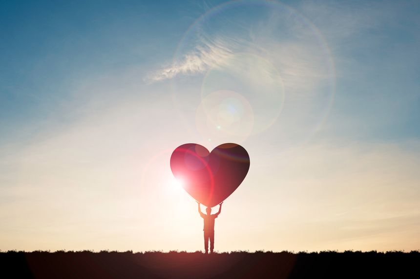 Silhouette man show two hand rise up and carrying heart with sunlight  and blue sky , Valentine 's day concept.