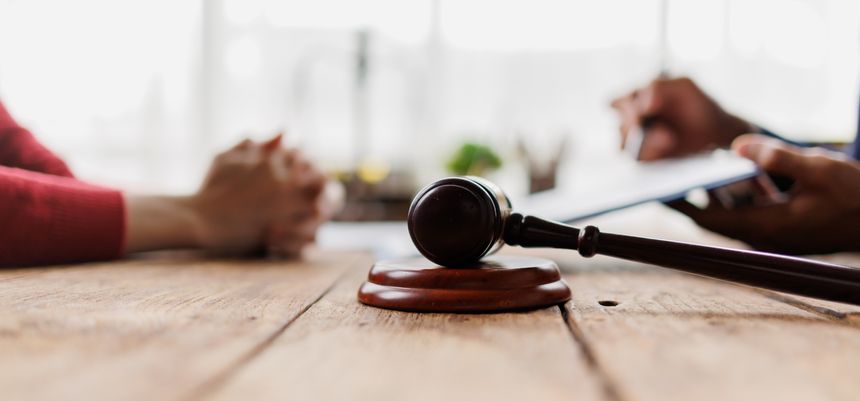 Gavel on a wooden table, symbolizing law and justice, while an attorney discusses legal agreements and advice with a client, focusing on court representation and dispute resolution