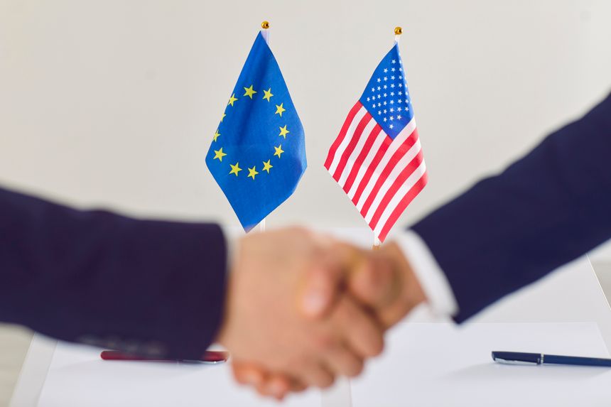 US cooperation and EU. Small flags of America and European Union on table in negotiating room during handshake that testifies to successful agreement. Blurred front. Selective focus.