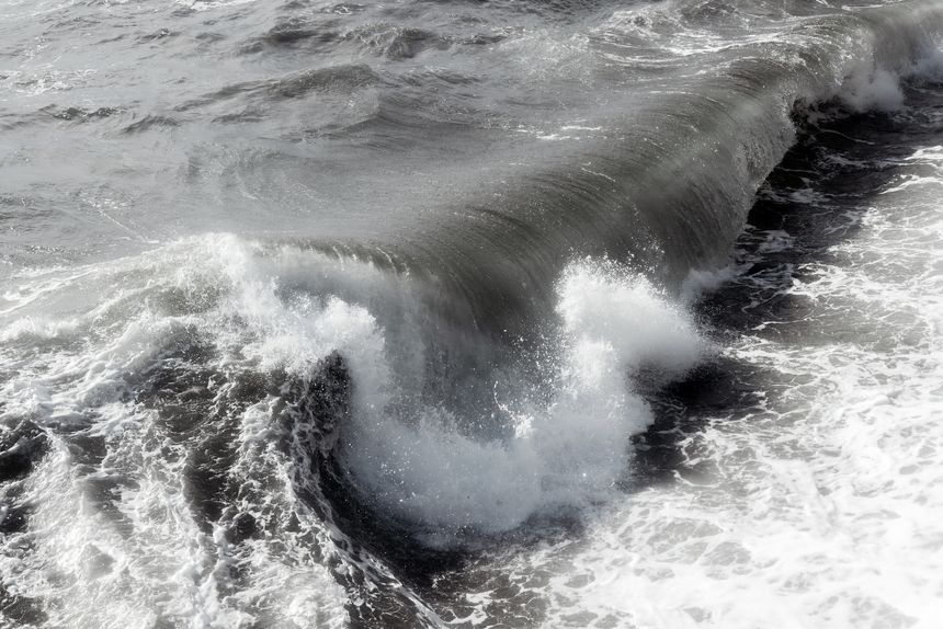 Powerful ocean wave crashing against the shore, creating a frothy spray of white water, showcasing the dynamic movement and energy of the sea in a dramatic coastal scene