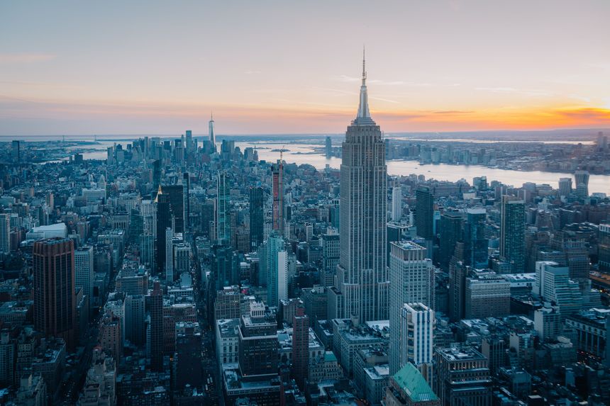 Aerial view of the New York City skyline at sunset featuring the Empire State Building and surrounding skyscrapers.