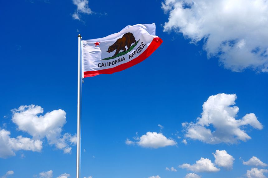 The flag of California flutters in the wind in a blue sky with white clouds