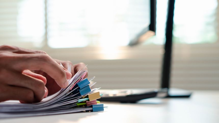 Office professional sorting a stack of paperwork beside a calculator, representing business management and data organization, administrative workload,compliance, deadlines, and business organization.