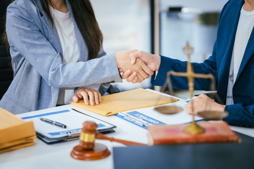 A male lawyer is shaking hands with a female client at a desk in a law office. They finalize a deal, agreeing on a court case settlement, ensuring justice is served