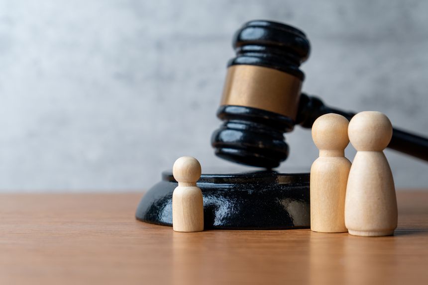 A wooden gavel stands next to three wooden peg dolls. Family law, guardianship, child custody, legal protection, and parental rights concept.