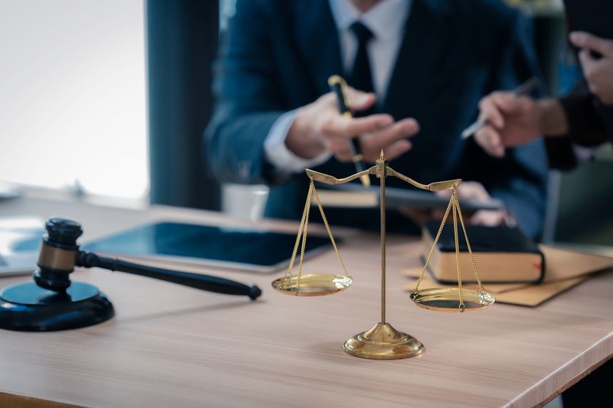 Law office with legal books and scales on table. Legal consultation: lawyer and client reviewing documents together. Representing trusts and legal proceedings. Close-up.