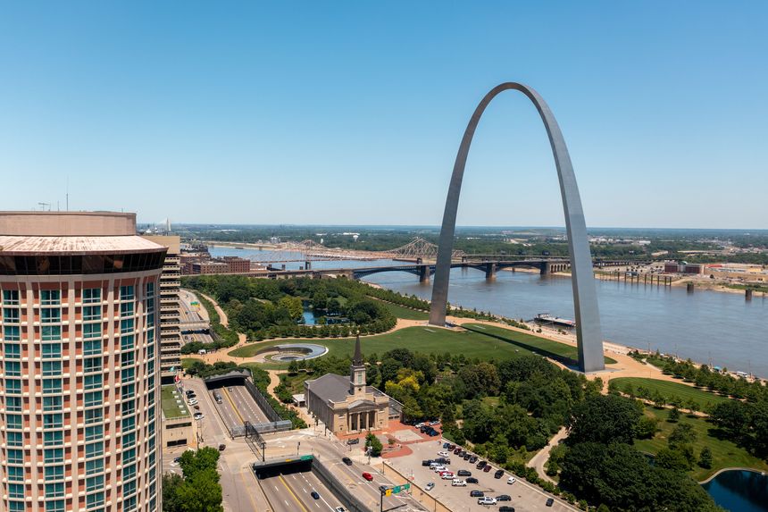 Drone view of the Gateway Arch with the Mississippi River, bridge, and surrounding park in downtown St. Louis.
