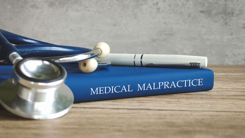 Stethoscope and a pen on a book titled MEDICAL MALPRACTICE, representing legal issues in healthcare.