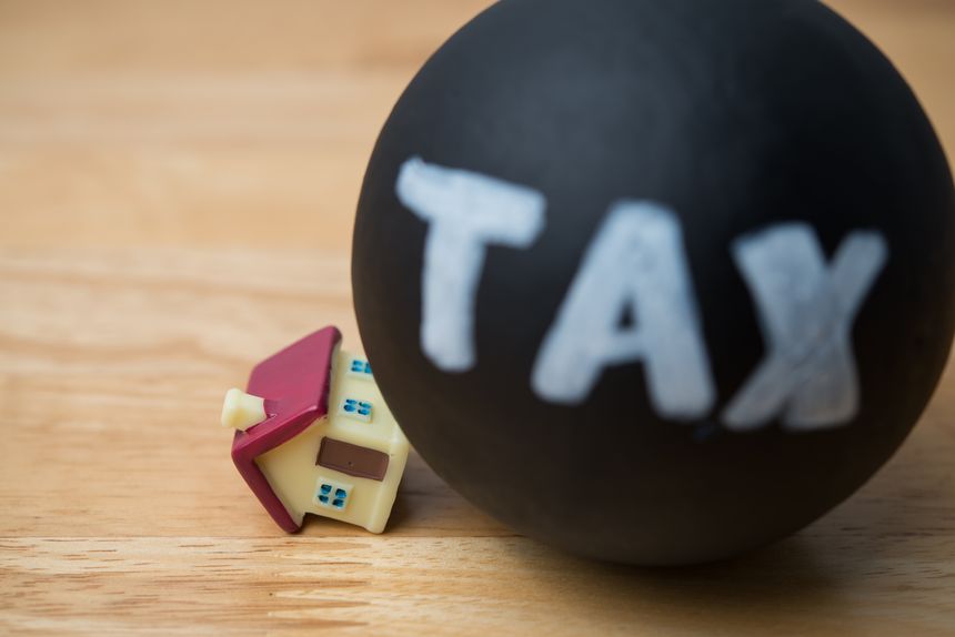 Heavy tax crash the house model on wooden table background. House building and land tax, property tax, financial planning, tax paying preparation in economy crisis and so on concept.